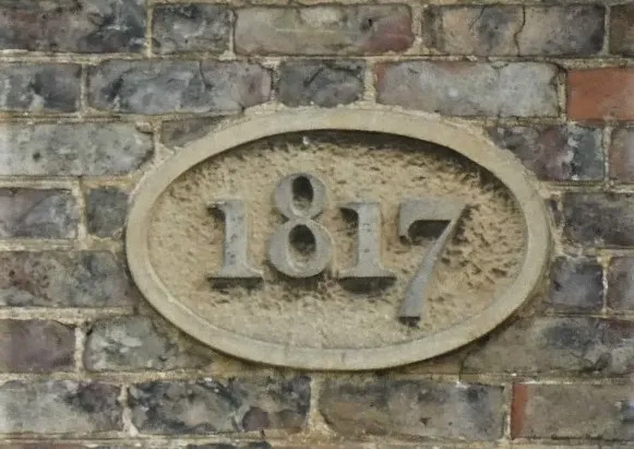 Oval stone plaque embedded in a weathered brick wall displaying the number 1817.