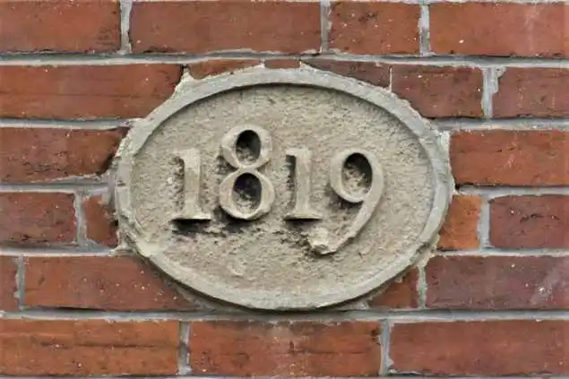 Oval stone plaque on a brick wall displaying the year 1819, weathered and carved.