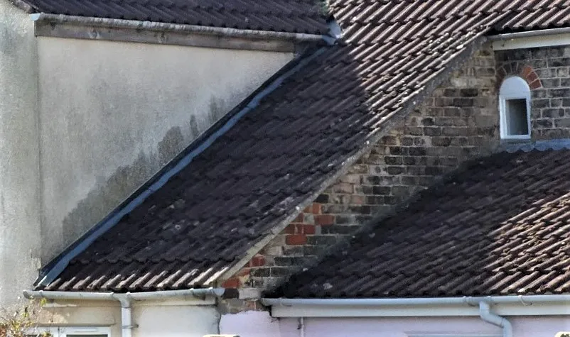 Row of dark tiled roofs overlapping a white wall, with a small arched window in the stone wall visible nearby.
