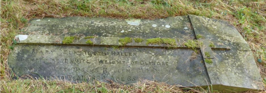 Flat, weathered grave marker lying in the grass, with moss and lichen growing on its surface and parts of the inscription faded away in a cemetery setting.