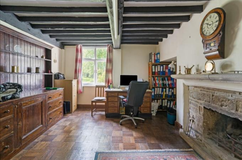 Cozy home office with a wooden desk, rolling chair, filing cabinets, and a fireplace on the right under a wall clock.
