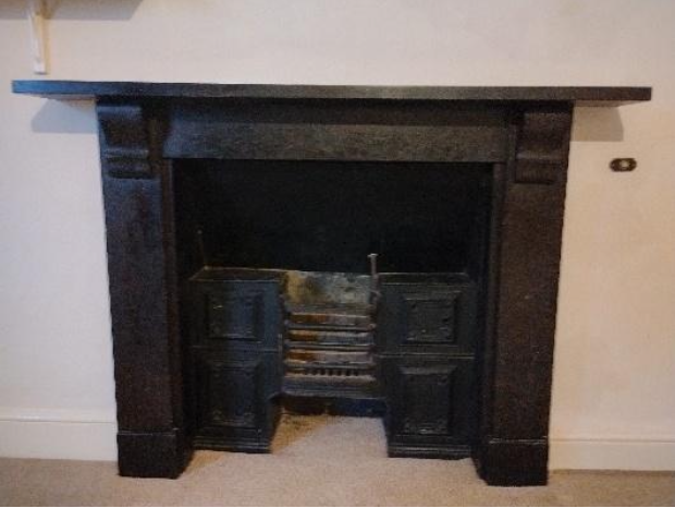 Dark wooden fireplace mantel with an old coal grate and iron insert against a white wall.