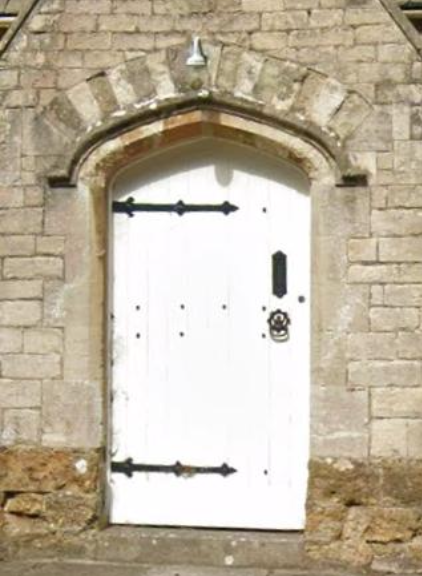 White wooden door set in a stone wall with an arched frame, iron hinges, and a door knocker.