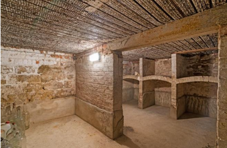 Stone-walled cellar with brick arches and built-in alcove storage in a dim basement setting