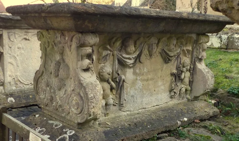 Stone urn or pedestal with weathered reliefs of small cherubic figures and draped scrollwork on a garden monument.