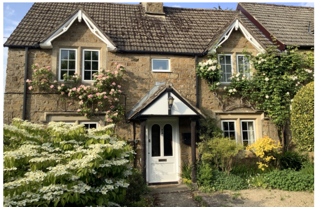 Stone cottage with climbing roses and a white front door under a small porch.