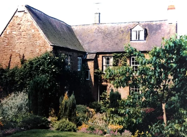 Brick cottage with ivy-covered walls and a lush garden in front.