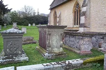 Weathered stone tombs in a churchyard beside a stone church, with green grass and moss.