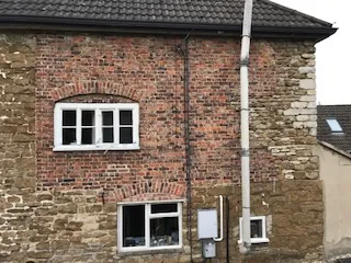 Brick exterior wall of a two-story house with white-framed windows, a rain gutter and visible utility meters.