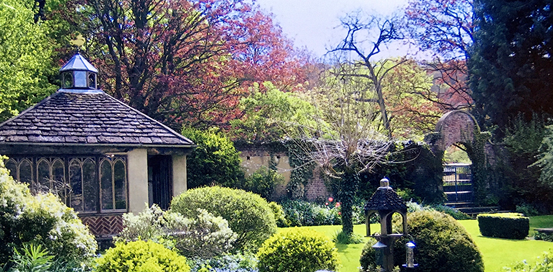 Manicured garden with a wooden gazebo, trimmed hedges, and colorful spring trees in the background.