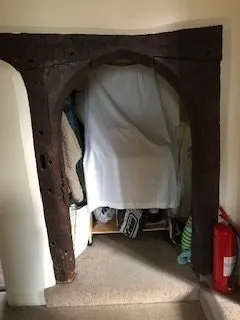 Doorway with a dark wooden frame leading to a small alcove; a white sheet covers a bulky object, with items and a red fire extinguisher on the right.
