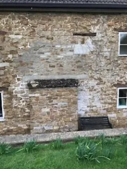 Weathered stone wall of a building with patchy plaster, a small window on the right, and a grassy foreground.